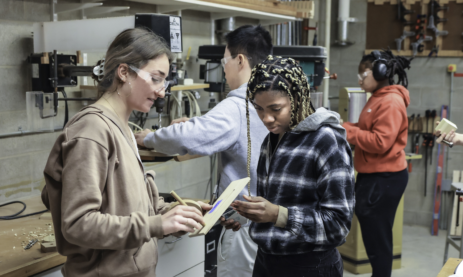 Cora Nagle ’24 discusses the music box she is making with Meleah Spriggs ’25. They are joined by Kevin Hsieh ’21 and Shante Frank ’25 in the woodworking lab of Stephen Blanchard.