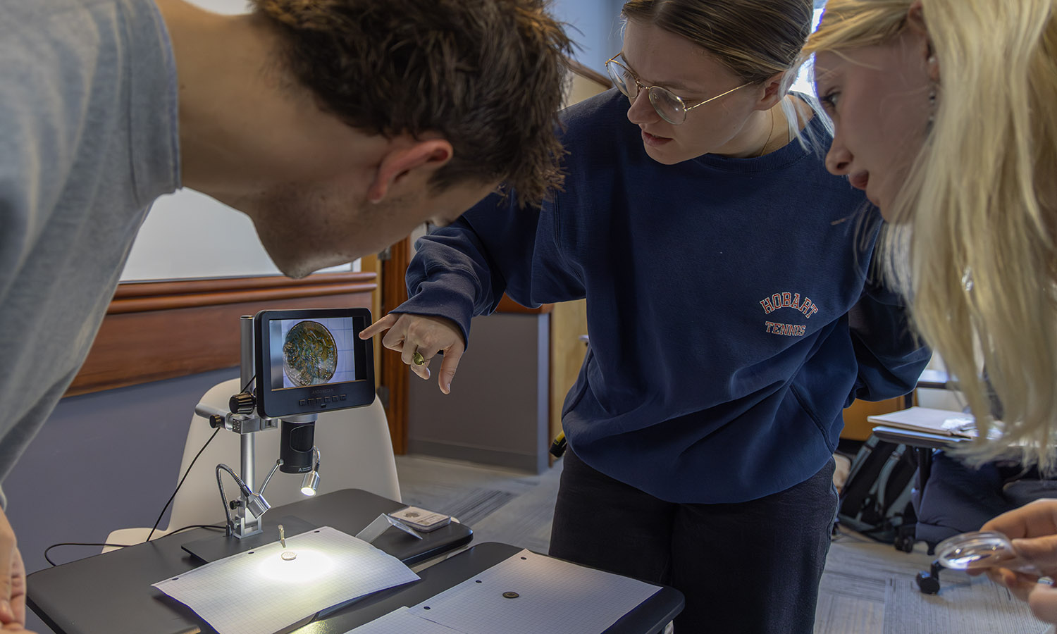 Joe Pariano ’27, Elizabeth Legg ’26 and Kim Wick ‘26 examine an Ancient Greek Coin from Ptolemaic Egypt (c. 200 BCE)  in Associate Professor of Greek and Roman Studies Jim Capreedy's "Ancient Epigraphy" course. 
