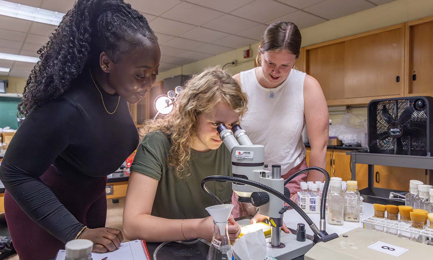 While working with Professor of Biology Kristy Kenyon, Ellean Macarthy ‘27, Genevieve Larkin ‘27 and Caroline Gannon ‘26 view anesthetized flies (Drosophila melanogaster) to determine if the loss of specific genes affects traits such as eye and body color. 