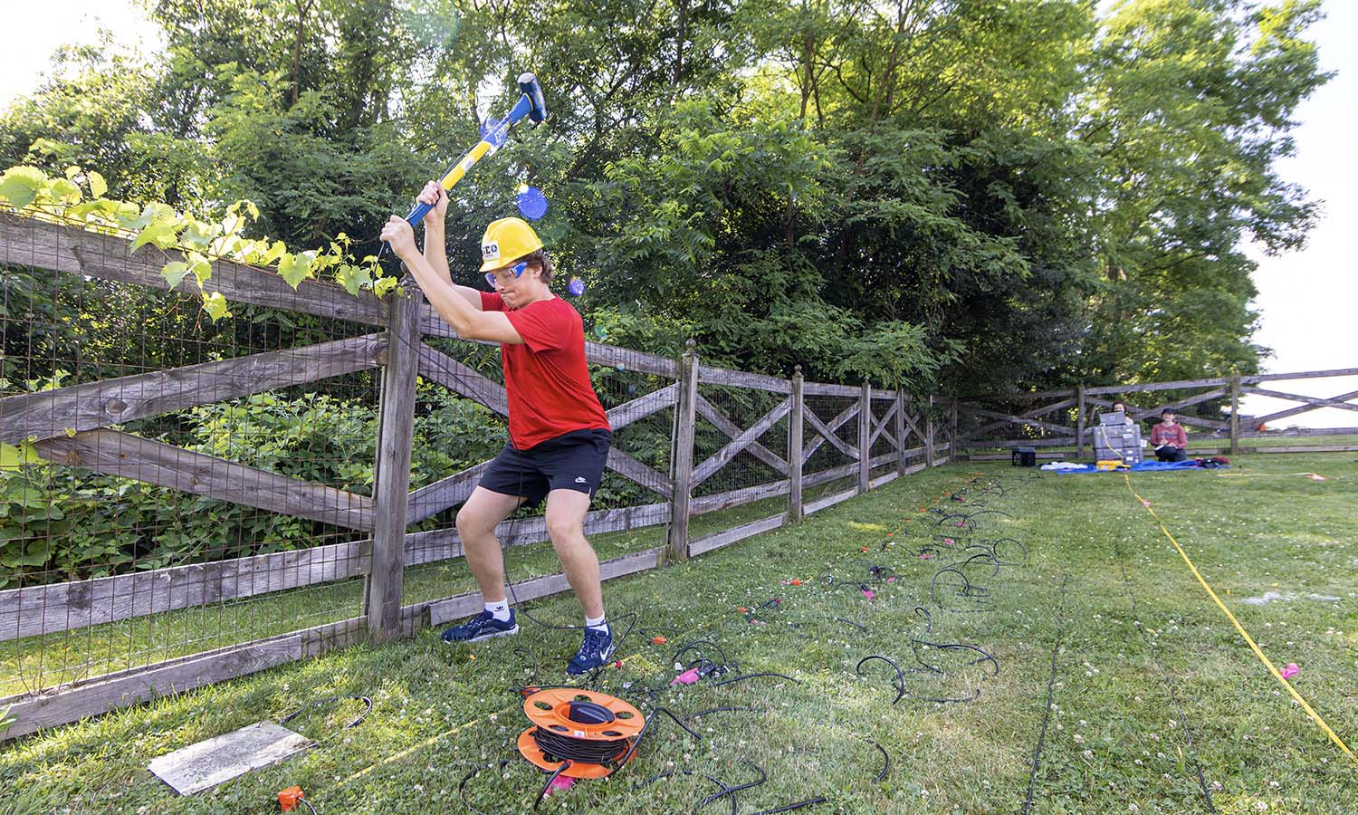 Noah DeLong '27 hits a strike plate with a sledge hammer, while Eloise Ruberti '27 and Associate Professor of Geoscience Tara Curtin record the seismic waves for a refraction survey they're conducting around Seneca Lake.