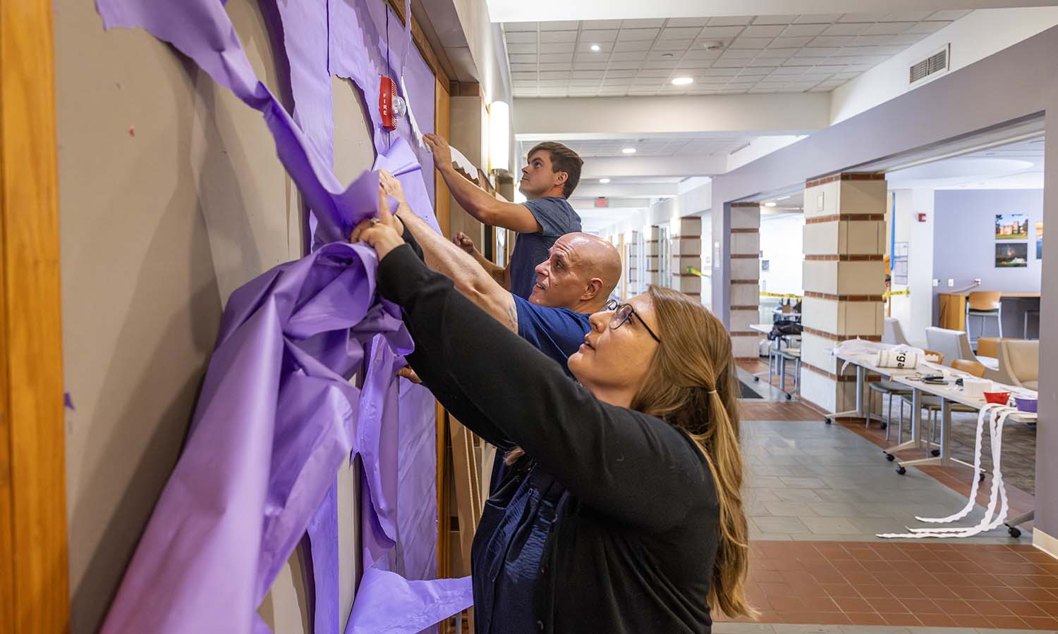 Graduate Assistant for Programming Evan Degraw, Director of Student Activities & Greek Life Ryan Steinberg and Associate Director of Student Activities Cari Bastian prepare a new poster wall in the Scandling Campus Center. 