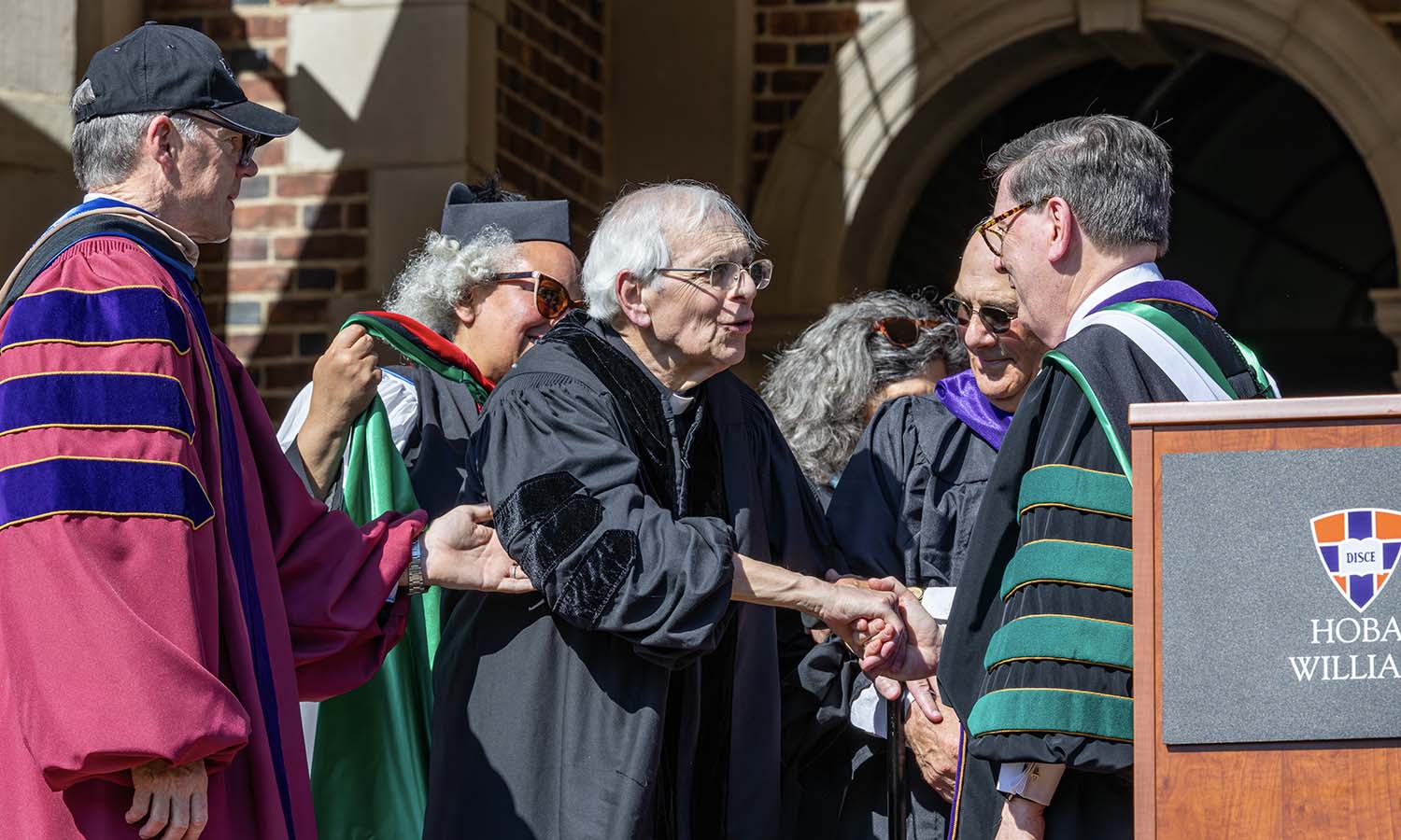 Father Thomas P. Mull D.D. ’26 receives an honorary doctorate of divinity surrounded by the staff of the Office of Spiritual Engagement and assisted by Board Chair Joe Stein ’86 and former Director of Athletics Mike Hanna ’68, P’99.   