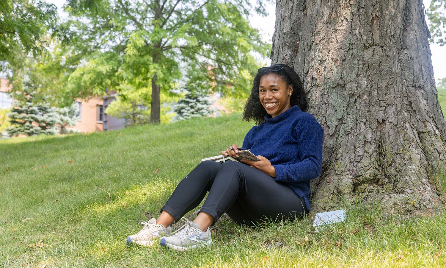 Gianna Hester ’27 sits under her favorite tree on the hill outside of McCormick House overlooking the William Smith soccer practice field.&nbsp; 