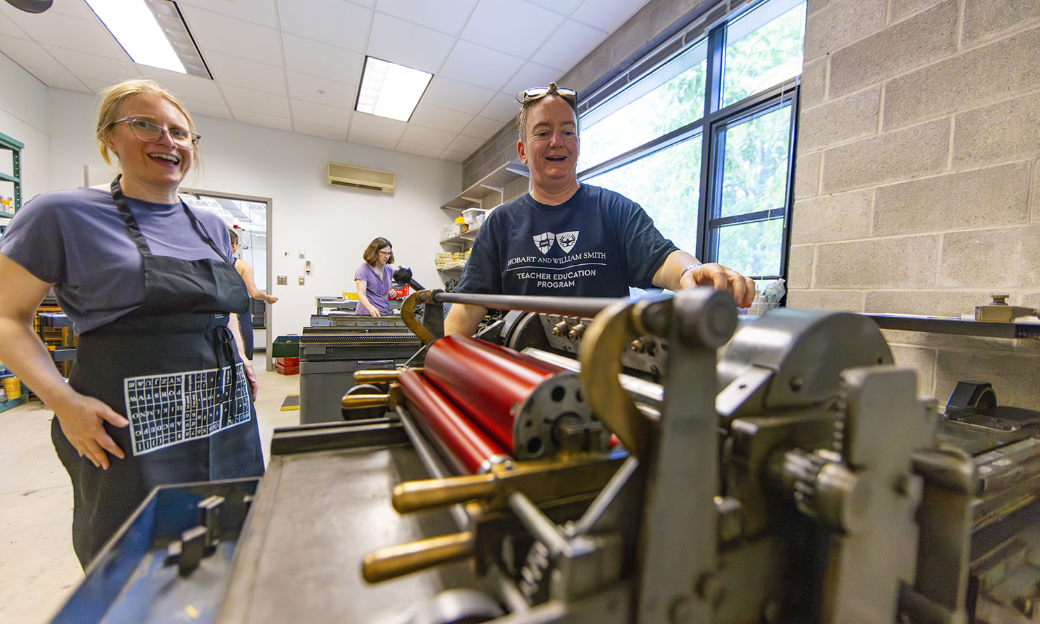 Director of the Wells Book Arts Center Mary Tasillo observes Director of Teacher Education Program Andie Huskie using a Vandercook proof press during a printing workshop in the Elliot Studio Arts Center.   