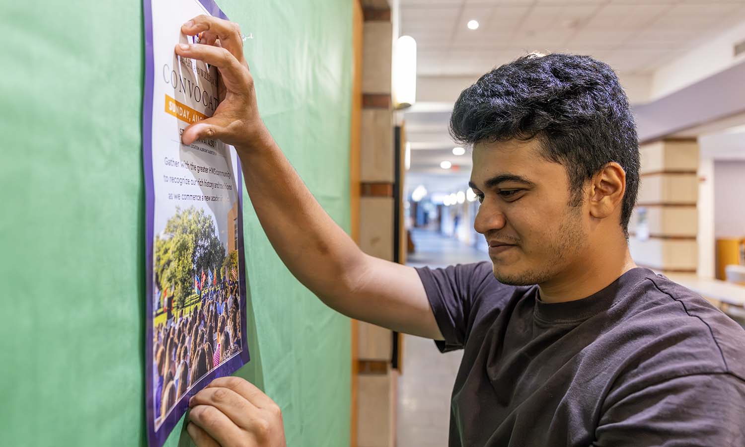 Azmain Shafin ’29 hangs up a poster in the Scandling Campus Center to promote Convocation. 
