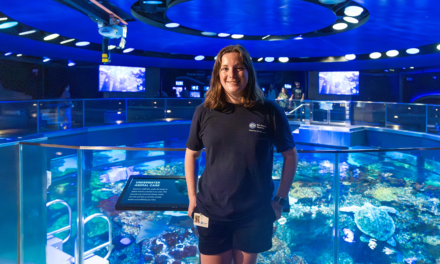 Kaleigh Boynton ’28 stands in front of the “Giant Ocean Tank” at the New England Aquarium, where she interned this summer.  
