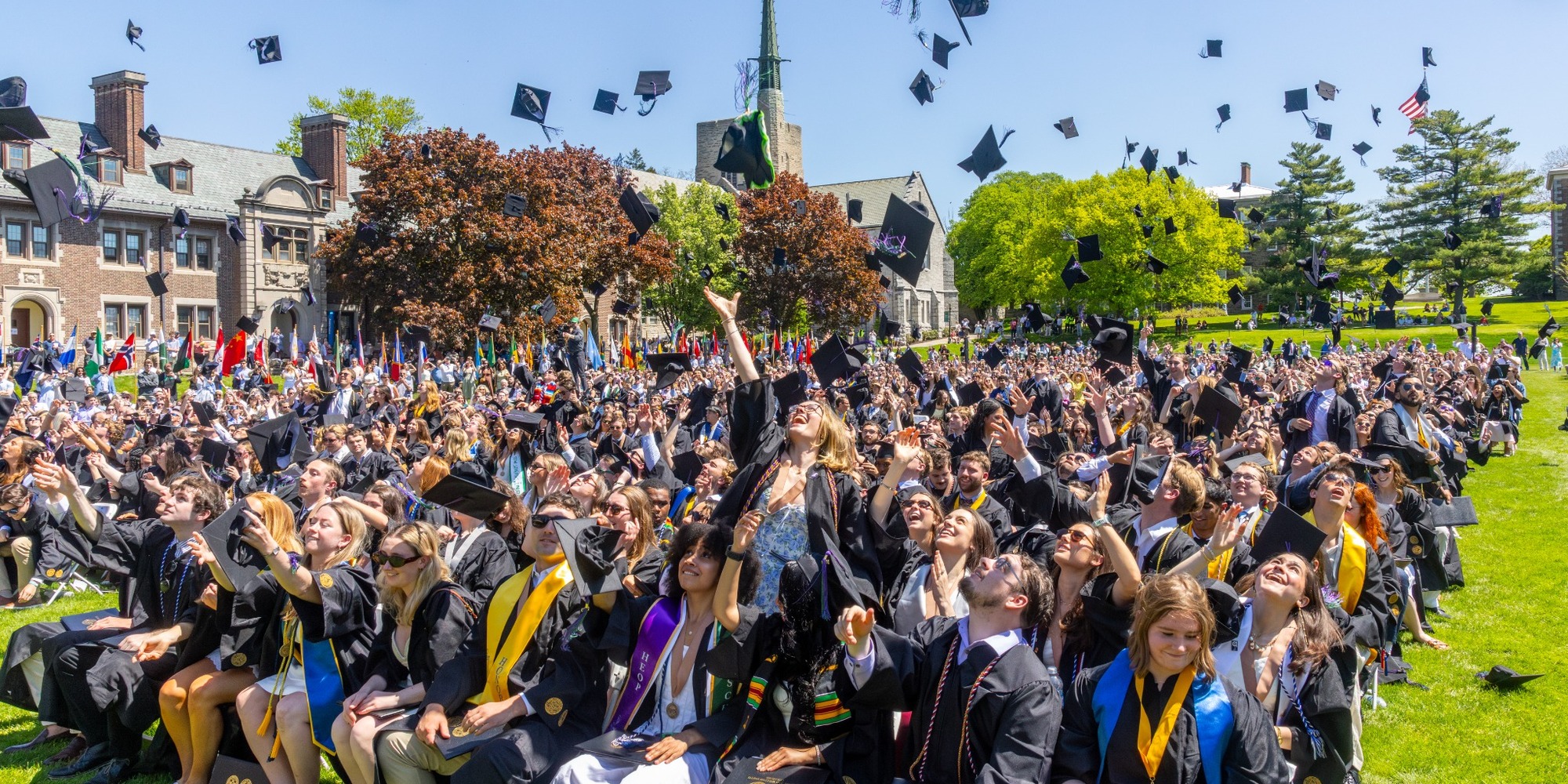 Graduates in caps and gowns throwing their mortarboards into the air on the Quad at Commencement