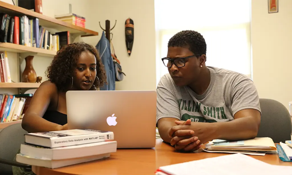 Student and professor gathered around a laptop.