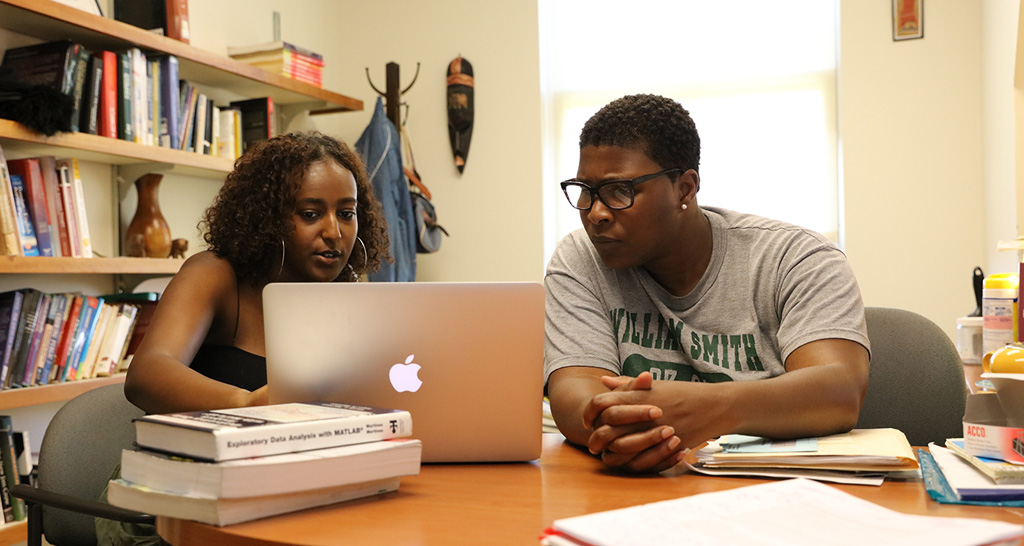 Student and professor gathered around a laptop.