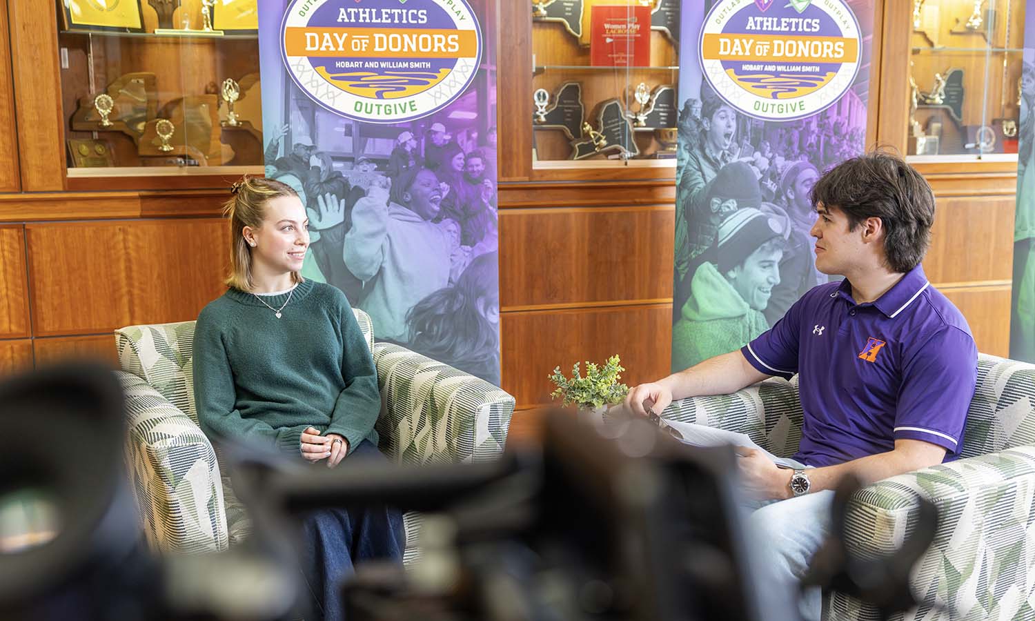 Two HWS students talk in front of Athletics Day of Donors banners